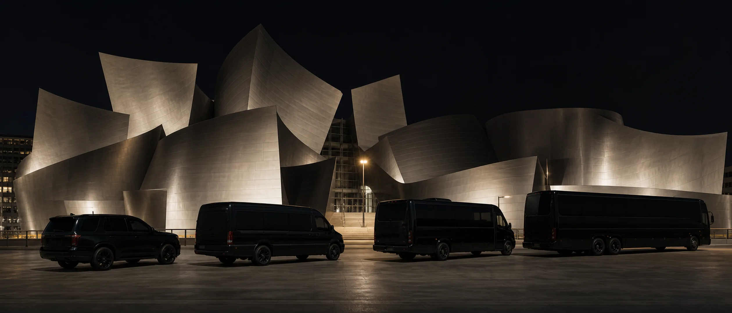 Four black vehicles are parked along a shallow arc beside Walt Disney Concert Hall.