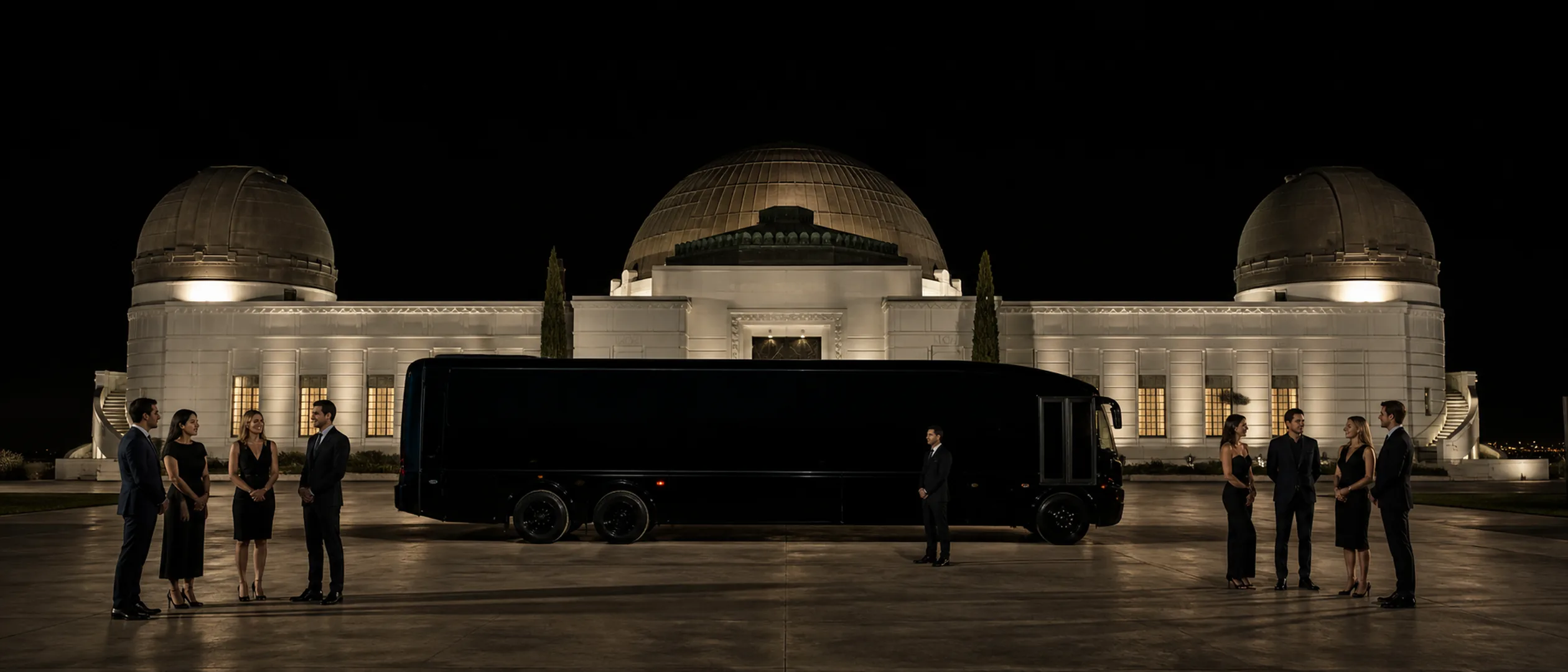 Eight travelers meet a chauffeur beside a black motorcoach below Griffith Observatory.