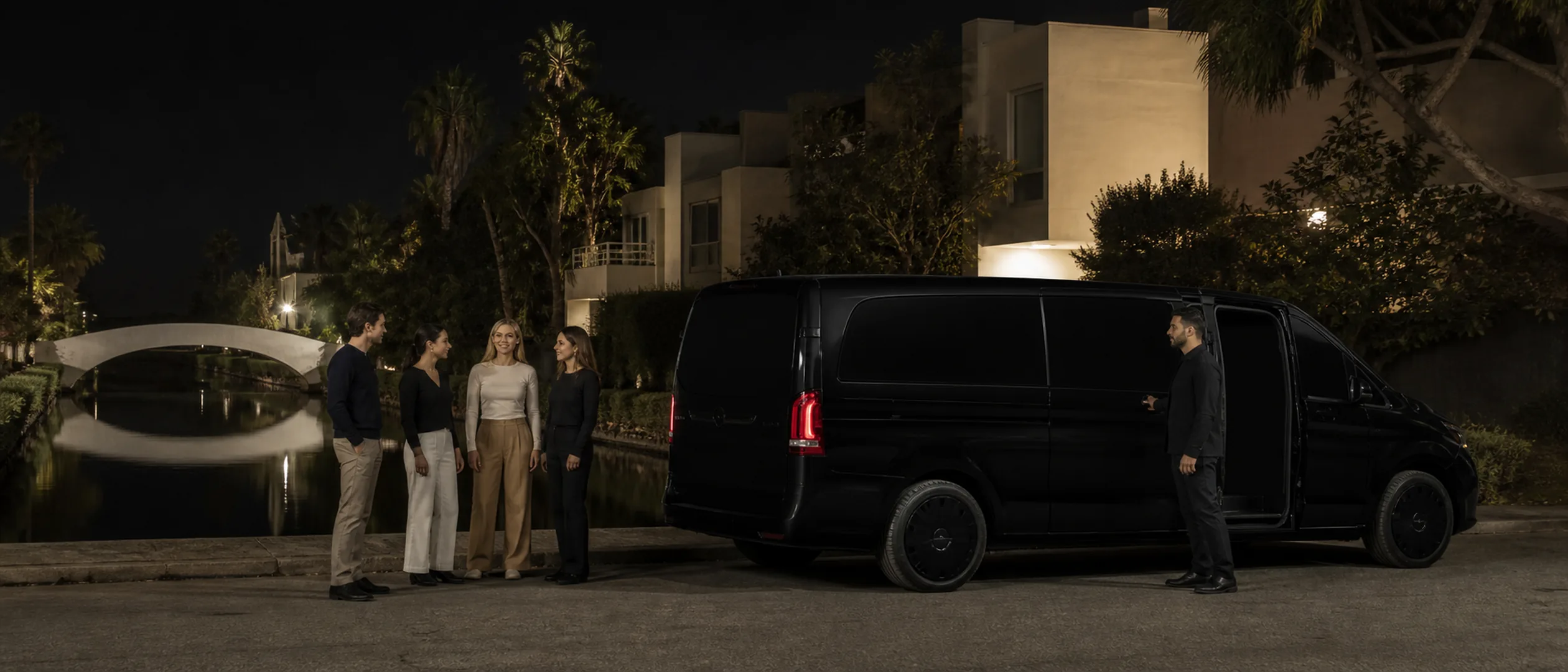 Four travelers meet a chauffeur beside a black passenger van near the Venice Canals in Los Angeles.